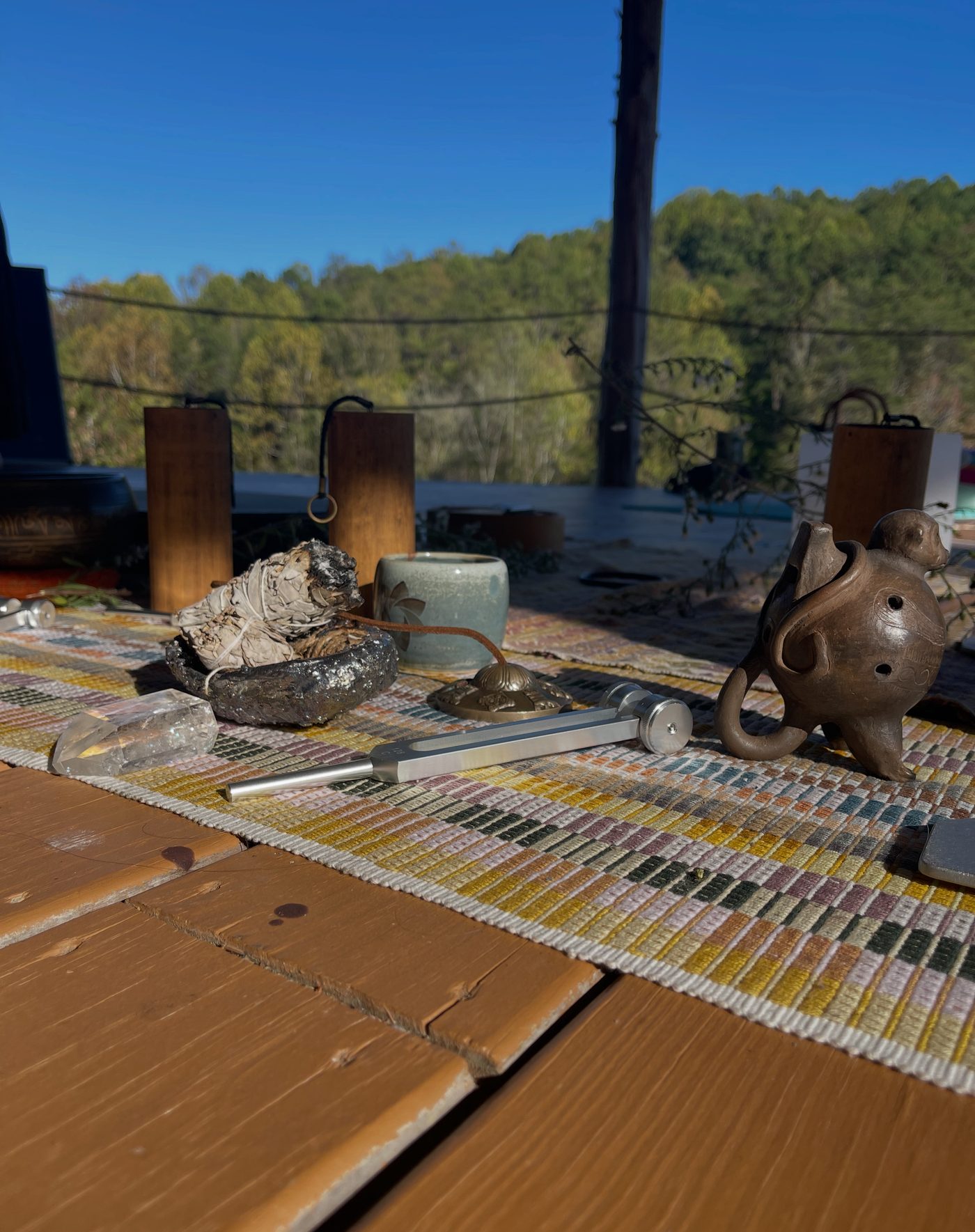 Meditation altar on the porch — sage bundle, crystal, tuning fork, and teapot on a woven runner