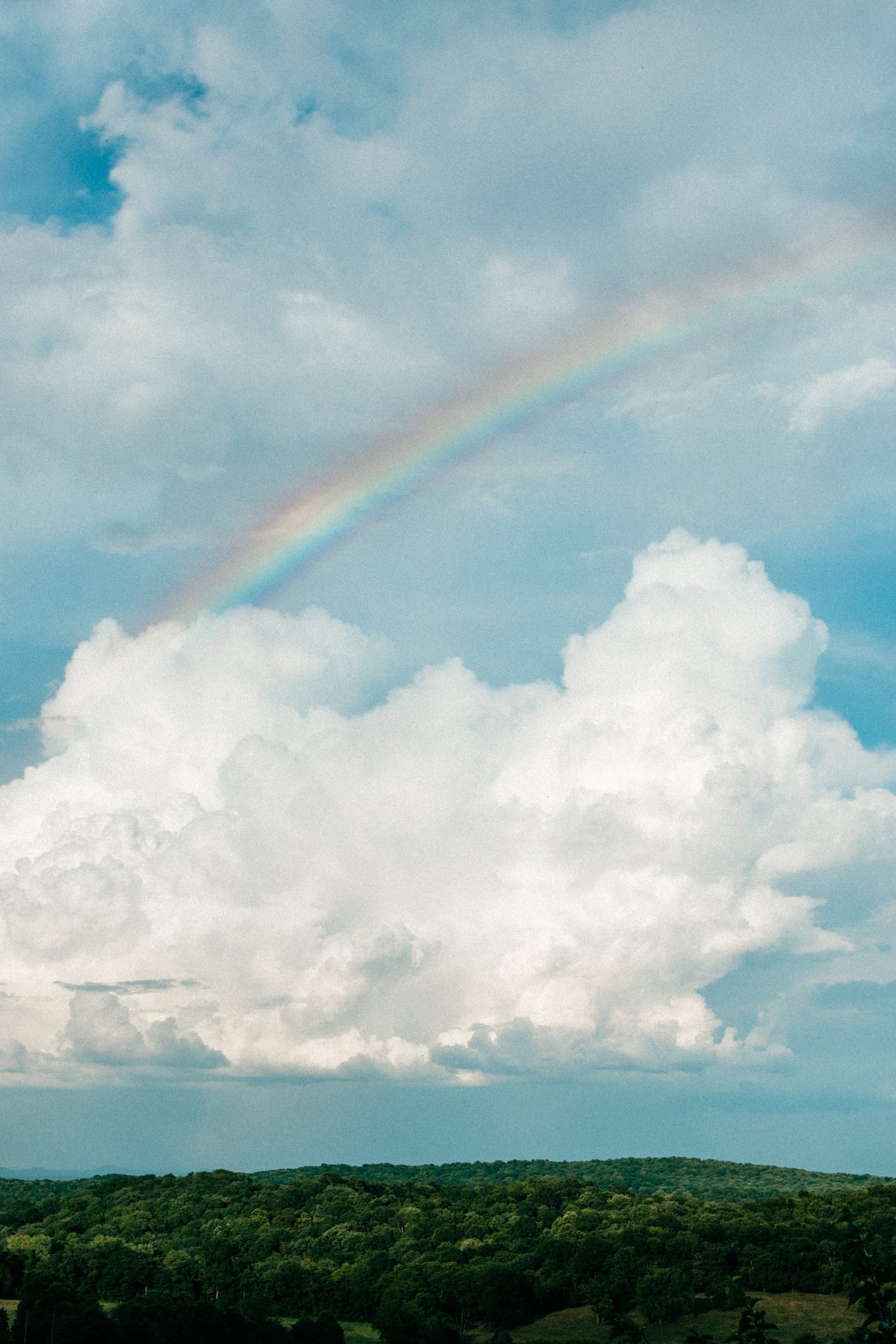 Rainbow arching over green Tennessee hills with billowing clouds